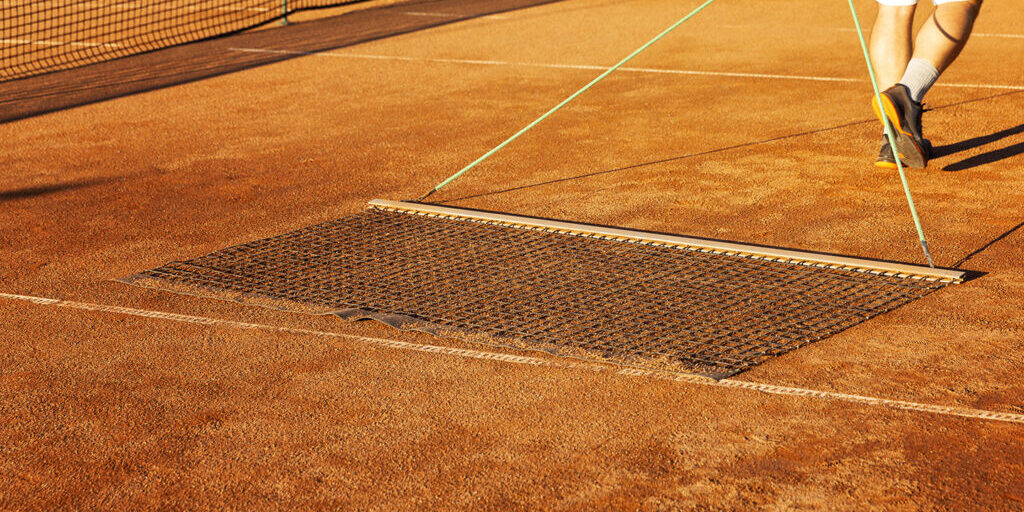 Preparing a tennis court for the match. Man aligns ground cover.