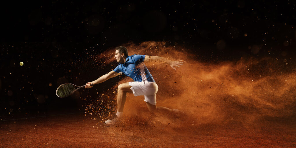 Male sportsman is playing tennis on an outdoor stadium with sand surface. He is wearing unbranded sports cloth and using unbranded sport equipment